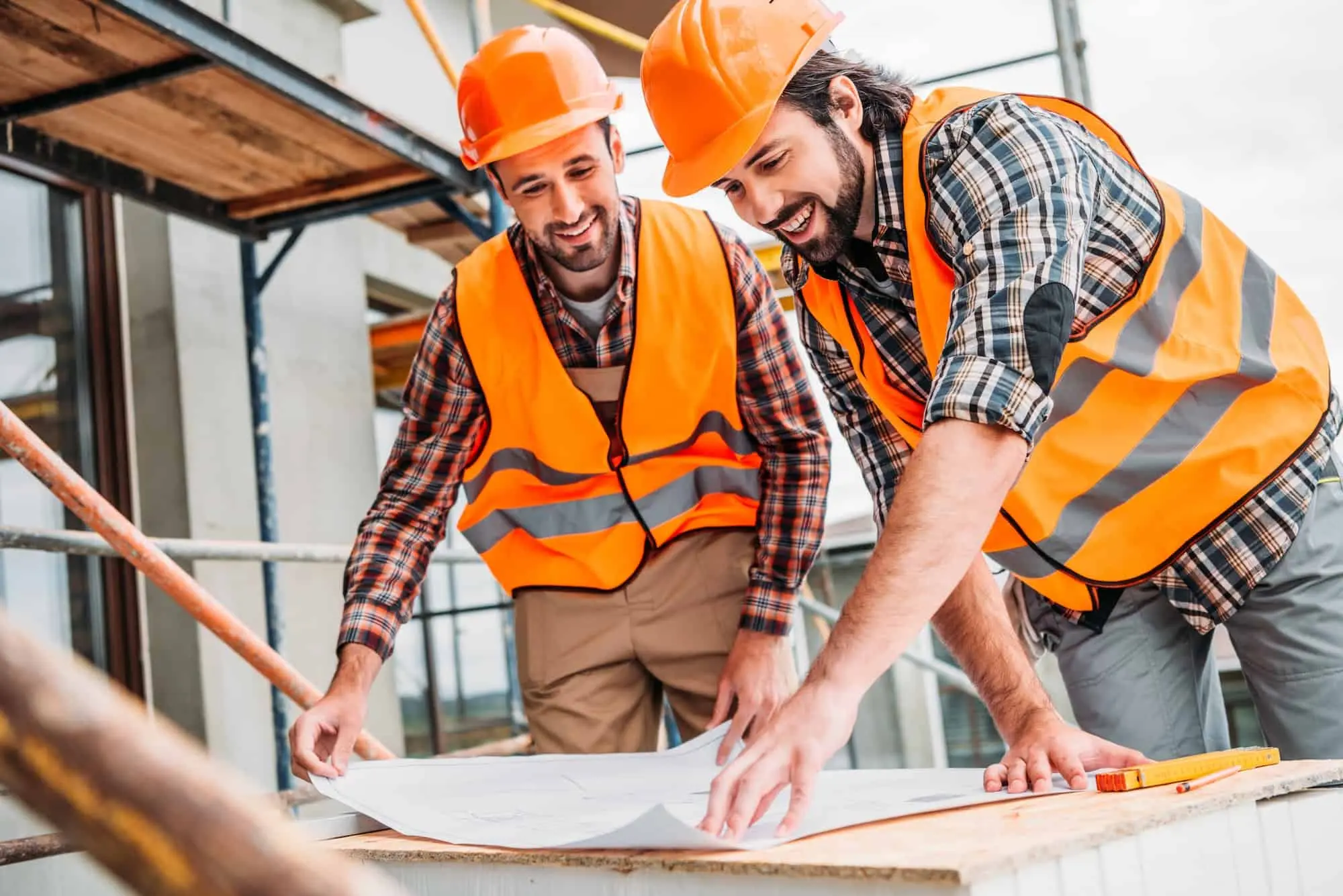 Two roofing contractors in safety gear reviewing blueprints on a construction site – Roof Repair Westchester team.