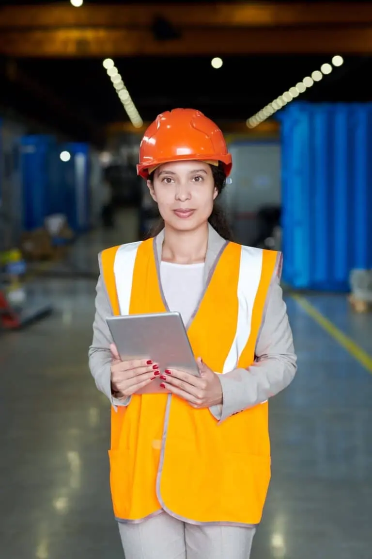 Female construction manager in safety gear holding a tablet at a job site – Roof Repair Westchester.
