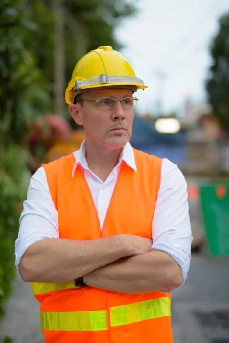 Male construction supervisor in yellow hard hat and orange safety vest overseeing a roofing project – Roof Repair Westchester.