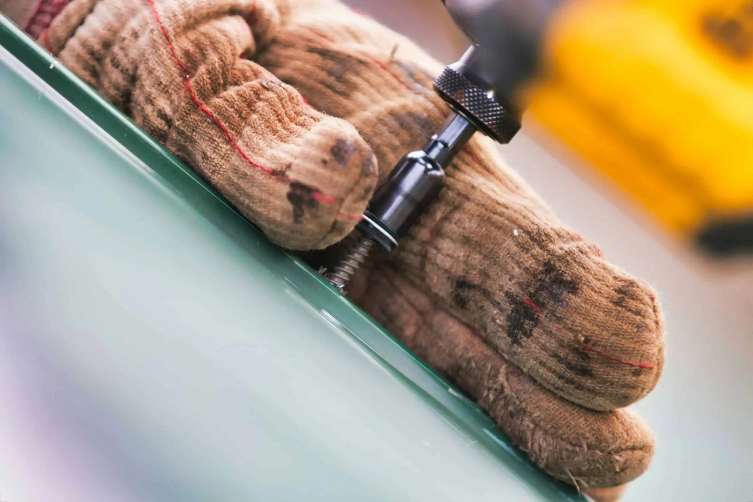 Close-up of a roofer’s gloved hand using a power drill on a metal sheet – Roof Repair Westchester.