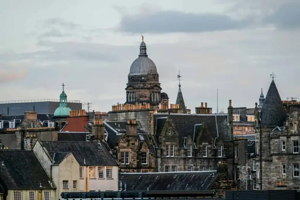 Historic European cityscape with stone buildings, rooftops, and a central dome under a cloudy sky.
