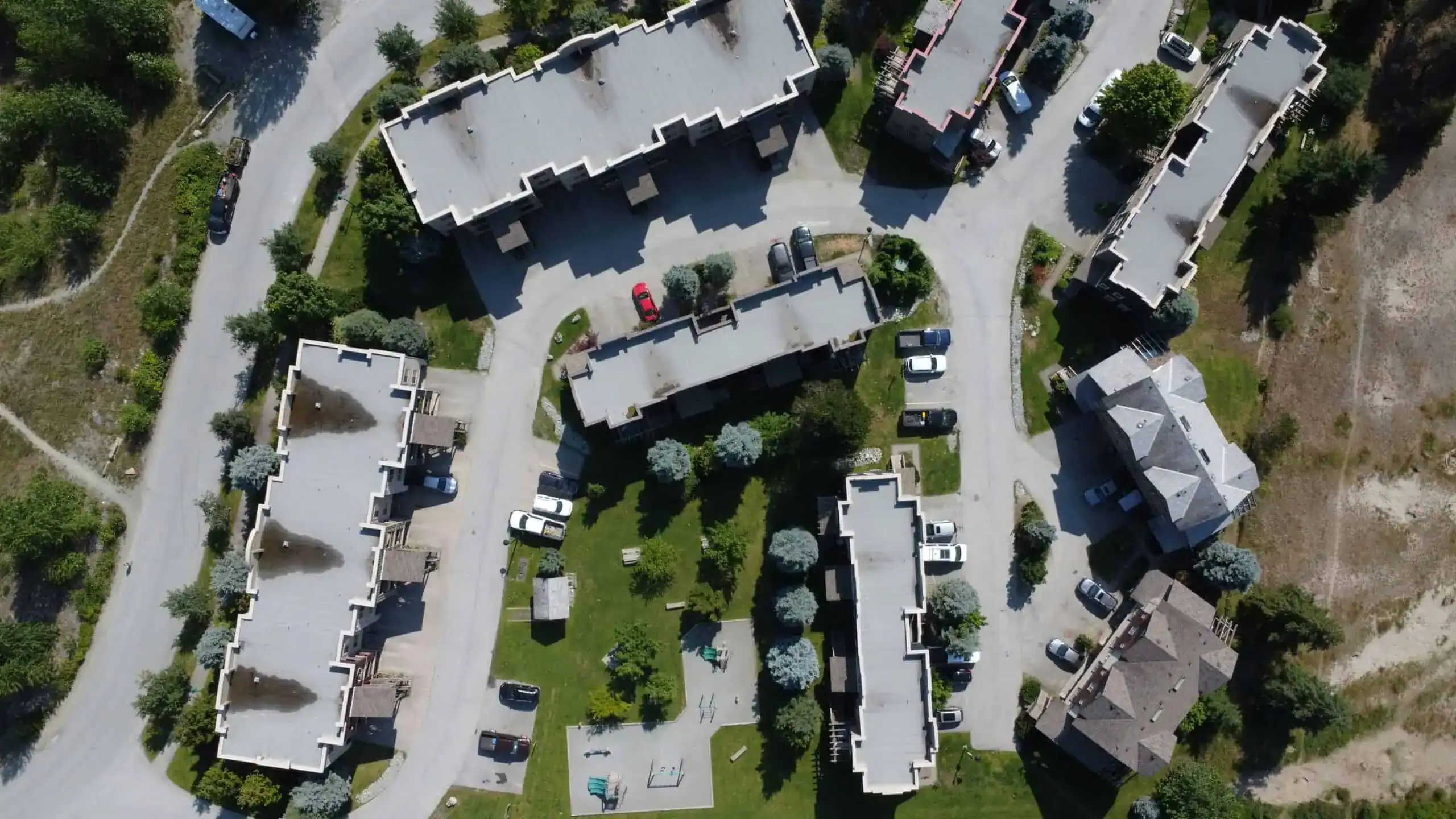 Aerial view of residential apartment buildings with flat rooftops, parking lots, and green landscaping.